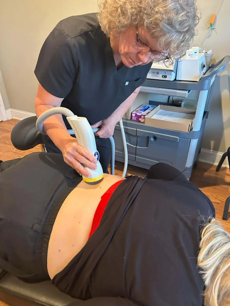 SoftWave vs shockwave therapy comparison shown during non-invasive lower back pain treatment by a healthcare provider.